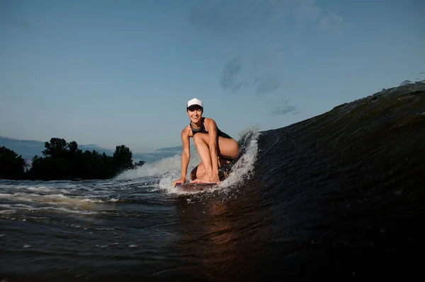 有魅力的妇女站在一膝上的 Wakesurf 上的树木和晴朗的天空的背景 — 图库照片