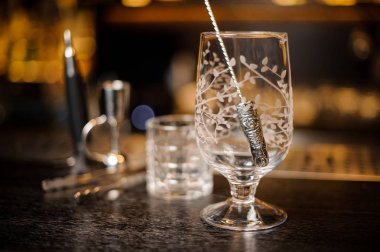 Empty cocktail glass with a steel spoon on the bar counter against blurred bright background clipart