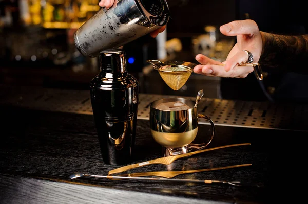 Barman pouring fresh and tasty summer drink from shaker into the vintage copper mug on bar counter
