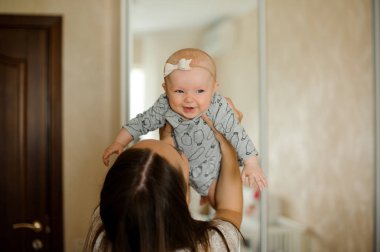 Genç Anne şirin ve mutlu yeni doğan bebek kız yatak odasında yukarı savurma ile oynarken