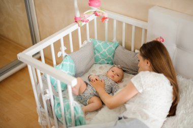 Sevimli küçük yeni doğan bebek kız oldukça beyaz ve mavi yatakta lulling mutlu anne