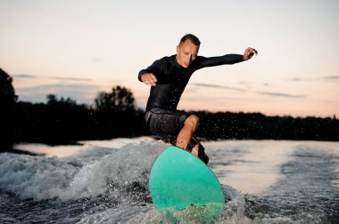 Siyah mayo de akşam nehirden aşağı sürme bir uyku modundan çıkarma tahtada atlama etkin wakesurfer