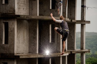 Bir slackline yüksek boş bina arka planı üzerinde dengeleme genç bir cesur adam arkadan görünüm