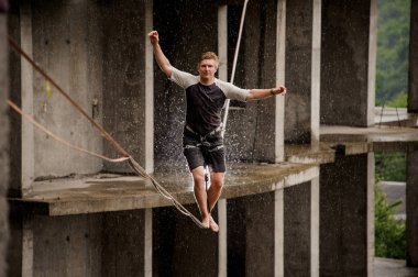 Genç adam bir slackline yüksek boş yaz gününde binanın arka planı üzerinde dengeleme cesur