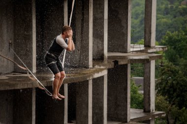 Bir slackline üzerinde duran ve yüzünü elleri boş bina karşı olan kapsayan genç adam