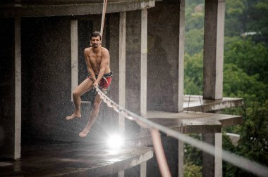 Üstsüz adam slackline yağmurlu günde boş binanın arka planı üzerinde dengeleme