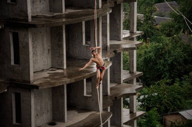 Atletik üstsüz adam slackline yağmurlu günde boş binanın arka planı üzerinde dengeleme