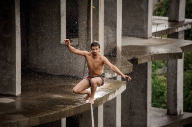 Güçlü cesur üstsüz adam slackline yağmurlu günde boş binanın arka planı üzerinde dengeleme