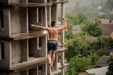 Üstsüz gencin bir slackline boş bina arka planı üzerinde yürüyen arkadan görünüm