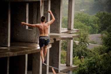 Bir slackline boş bina arka planı üzerinde yürüyen cesur üstsüz gencin arkadan görünüm