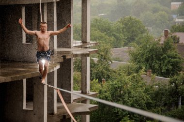 Bir slackline üzerinde yürüme ve yetiştirme cesur adam yağmurlu günde boş bina karşı eller