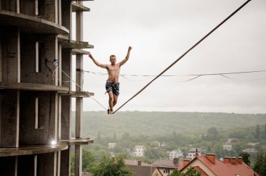 Cesur adam yağmurlu yaz gününde bir slackline boş bina ve gökyüzü karşı yüksek üzerinde dengeleme