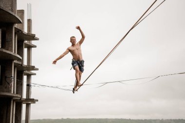 Korkusuz adam bir slackline boş bina ve gökyüzü karşı yüksek üzerinde yağmurlu yaz gününde Dengeleme