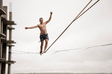 Güçlü cesur adam yağmurlu yaz gününde bir slackline boş bina ve gökyüzü karşı yüksek üzerinde dengeleme