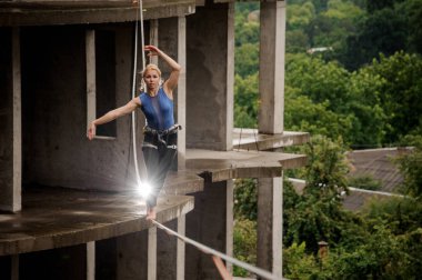 Bir slackline yüksek boş yaz gününde binanın arka planı üzerinde dengeleme aktif ve cesur kadın