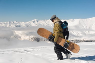 kar Dağları'nın arka plan üzerinde elinde bir snowboard ile sıcak Kayak ekipman erkek dağcı yürür