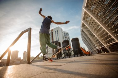 Arkadan görünüm etkin gencin arka planı şehir bina kaykay üzerinde yaz gününde atlama