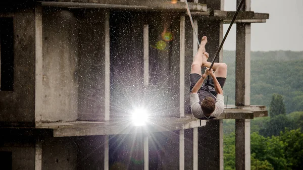 Young and brave man balancing on a slackline against the background of high empty building on rainy day