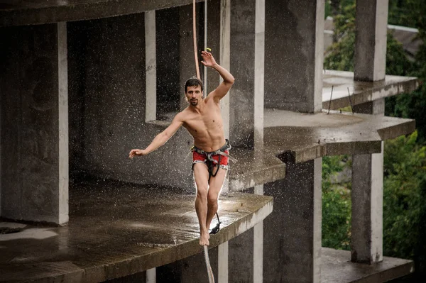 Güçlü korkusuz üstsüz adam slackline yağmurlu günde boş binanın arka planı üzerinde dengeleme