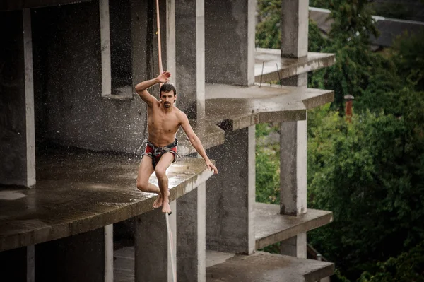 Bir slackline yağmurlu günde boş binanın arka planı üzerinde yürüyen güçlü korkusuz üstsüz adam