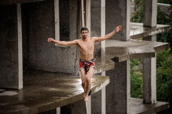 Üstsüz bir slackline yağmurlu günde boş binanın arka planı üzerinde yürüyen adam