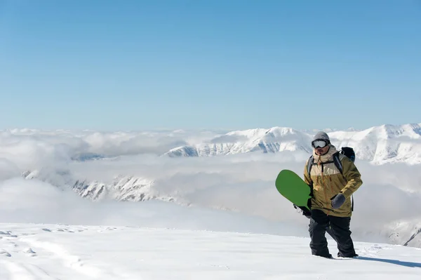 男子在滑雪设备 戴护目镜和绿色滑雪板在他的手徘徊在雪地上的膝盖深 — 图库照片