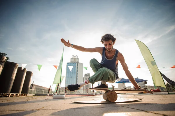Young smiling active man keeping balance on the wooden board against the background of city buildings on summer day