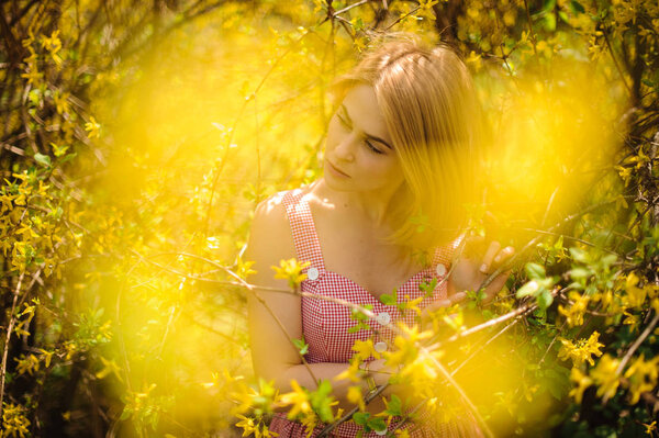 Young beautiful blond woman dressed in a pink dress standing near the blurred yellow blooming tree