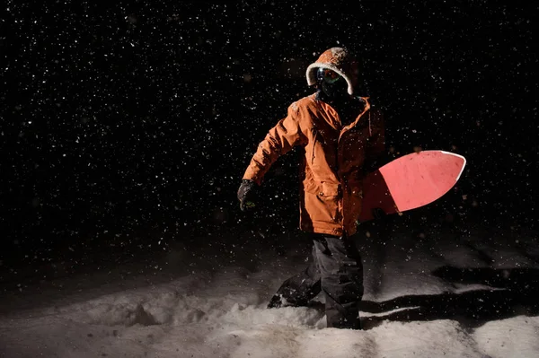 Man walking with the snowboard in the mountain in the night in the poplar tourist resort in Gudauri, Georgia