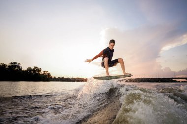 Genç çekici adam wakeboard Motorbot göl ve köprü arka plan üzerinde yüksek dalga üzerinde atlama