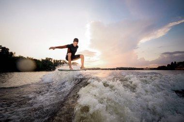 Genç çekici adam wakeboard Motorbot bir göl arka plan üzerinde yüksek dalga sürme