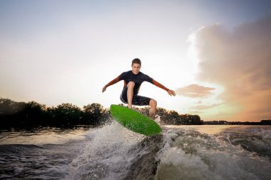 Yeşil wakeboard Motorbot bir göl arka plan üzerinde yüksek dalga yapma atlama genç çekici adam