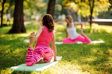 Parlak yeşil çimenlerin üzerinde bir parkta yoga egzersizleri yapıyor güzel kadının arkadan görünüm