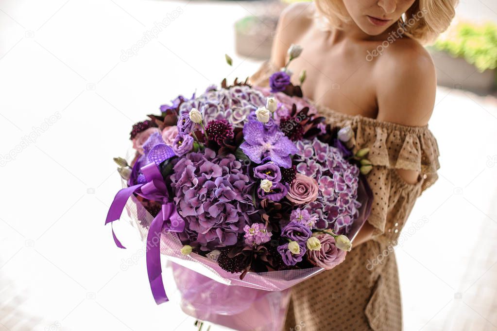 Woman in beige dress holding a big bouquet of flowers in bright and soft purple tones