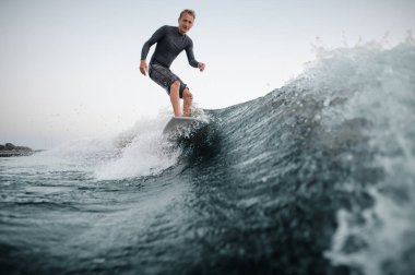 Önalan ile bir mutlu bir adam wakesurfing o aşağı arka planı gri gökyüzü üzerinde bir mavi dalga