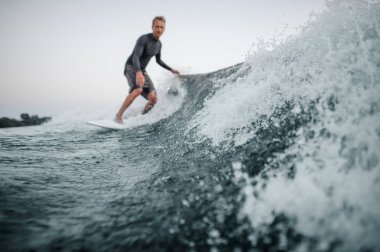 Mavi sıçramasına dalga önalan ile bir adam wakesurfing o aşağı arka planı gri gökyüzü üzerinde bir odak