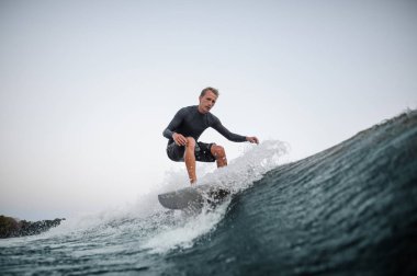 Açık gökyüzü arka planı mavi dalga aşağı gemide genç adam wakesurfing.