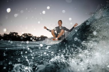 Lotus poz dalga damla sıçramasına odaklı mavi zemin üzerine kurulu oturup mutlu wakesurfer