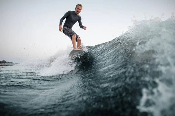 Önalan ile bir mutlu bir adam wakesurfing o aşağı arka planı gri gökyüzü üzerinde bir mavi dalga