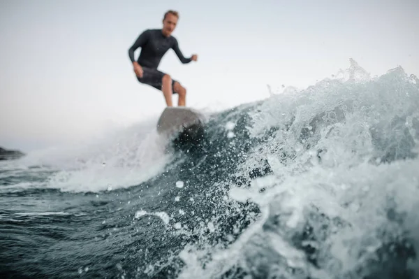 灰色の空を背景にそれを男の Wakesurfing と前景に焦点を当てるのブルー ウェーブ — ストック写真