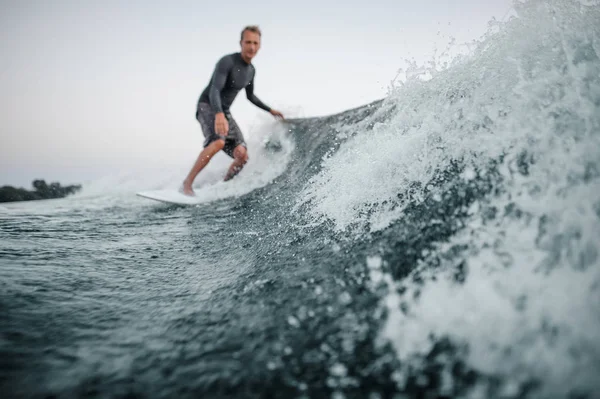 Mavi sıçramasına dalga önalan ile bir adam wakesurfing o aşağı arka planı gri gökyüzü üzerinde bir odak