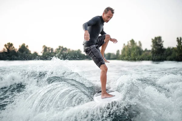 Profesyonel wakeboarder mayo açık gri gökyüzü ve ağaçlar arka planı mavi su aşağı sürme