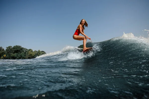 ボード上前景とヤングの金髪の女性 Wakesurfing 背景に青い波に高 — ストック写真