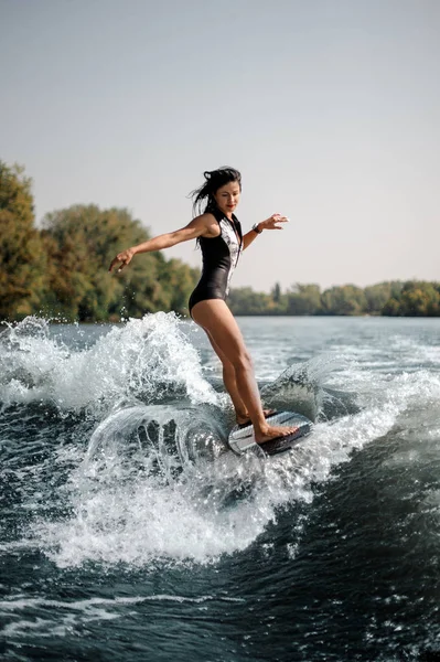 性感和活跃的黑发妇女 Wakesurfing 在蓝色的水在阳光明媚的一天板上 — 图库照片