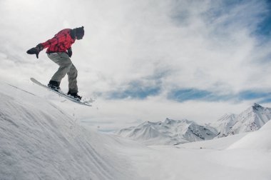 adam sıcak Kayak dişli snowboard yaparken karşı bir karla kaplı dağ zirveleri karlı bir dağ üzerinden atlıyor