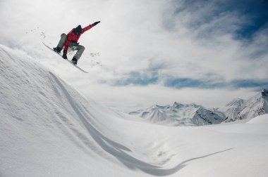 adam sıcak Kayak dişli mavi snowboard yaparken mavi bir gökyüzü ve karla kaplı dağ zirveleri karlı bir dağ üzerinden atlıyor