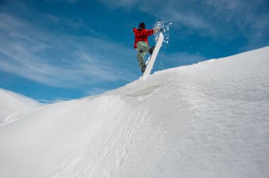 adam sıcak Kayak dişli mavi snowboard yaparken mavi bir gökyüzü ve karla kaplı dağ zirveleri karlı bir dağ üzerinden atlıyor