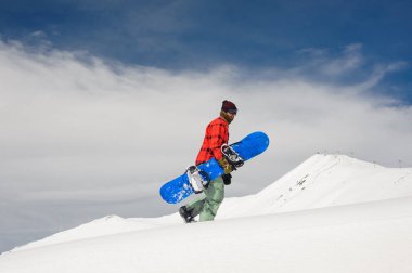Genç erkek snowboard snowboard onun elinde ile tepeye dağ ve açık mavi gökyüzü arka plan üzerinde yürüme