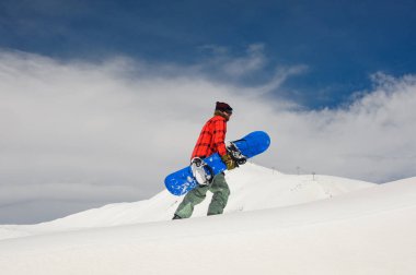 Genç snowboard snowboard onun elinde ile tepeye dağ ve açık mavi gökyüzü arka plan üzerinde yürüme
