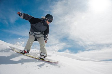 Dağ yokuş aşağı dağ ve açık mavi gökyüzü arka plan üzerinde çalışan genç kadın snowboard